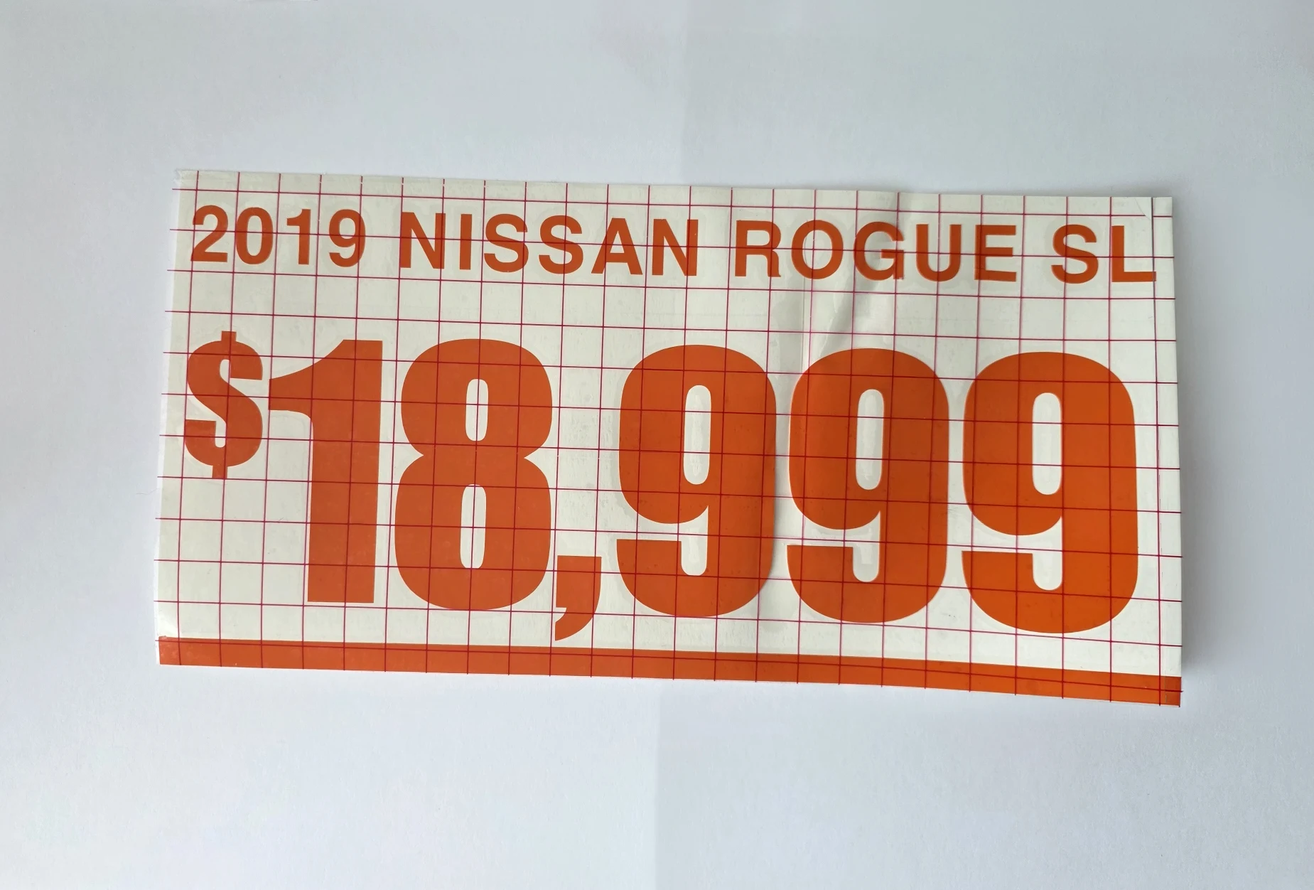 Full orange year, Nissan Rogue model and price sample held in position beneath gridded transfer tape