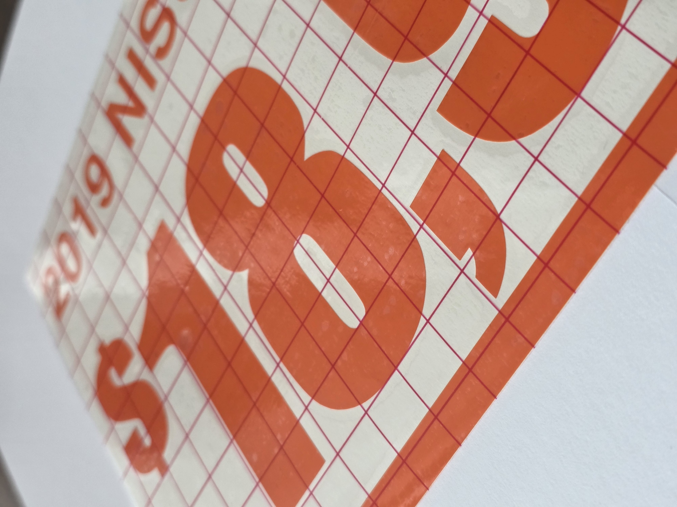Close-up of orange cut-vinyl price characters beneath gridded transfer tape