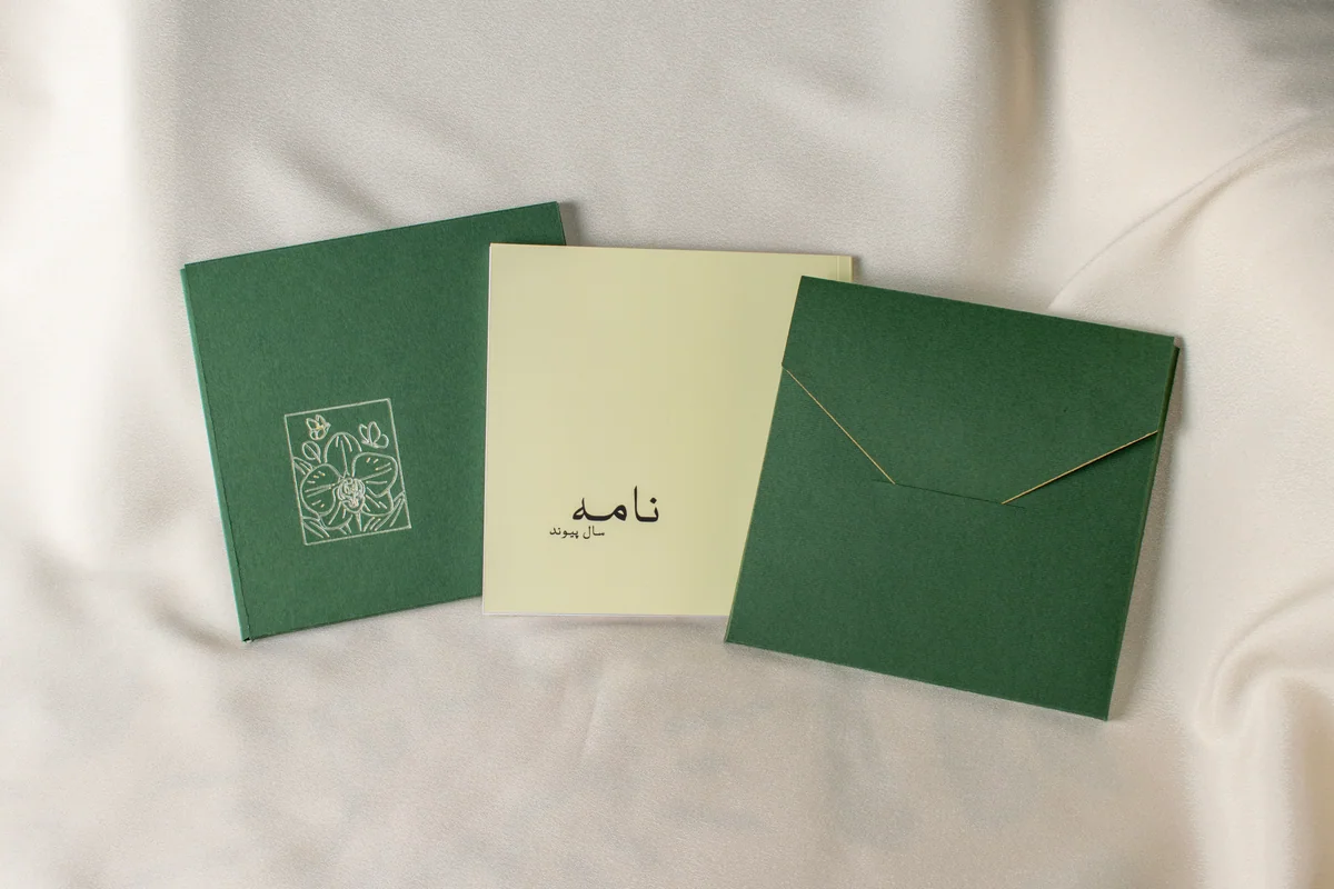 Avenoir-printed and bound anniversary book presented with a dark green custom folio featuring an embossed floral detail and a coordinating envelope