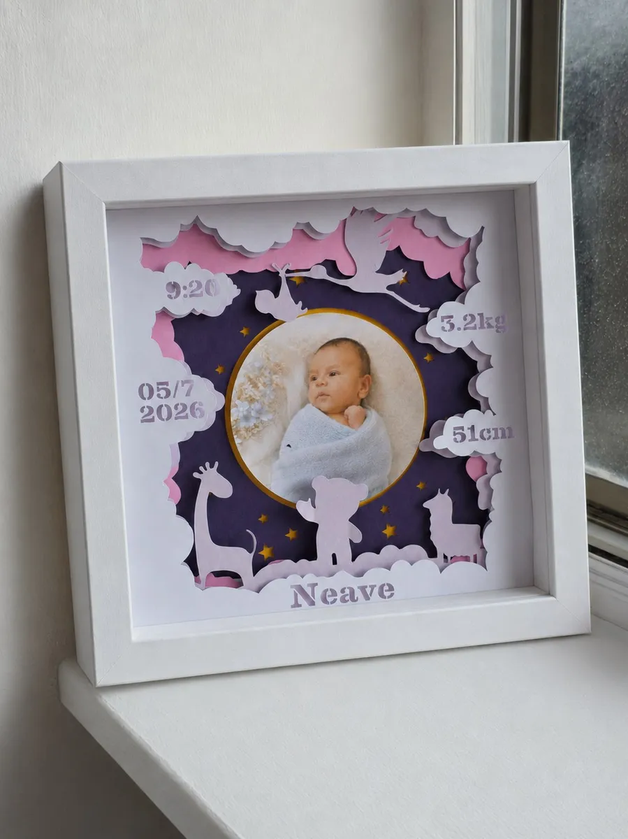 Personalized layered paper newborn keepsake displayed in a white shadow-box frame