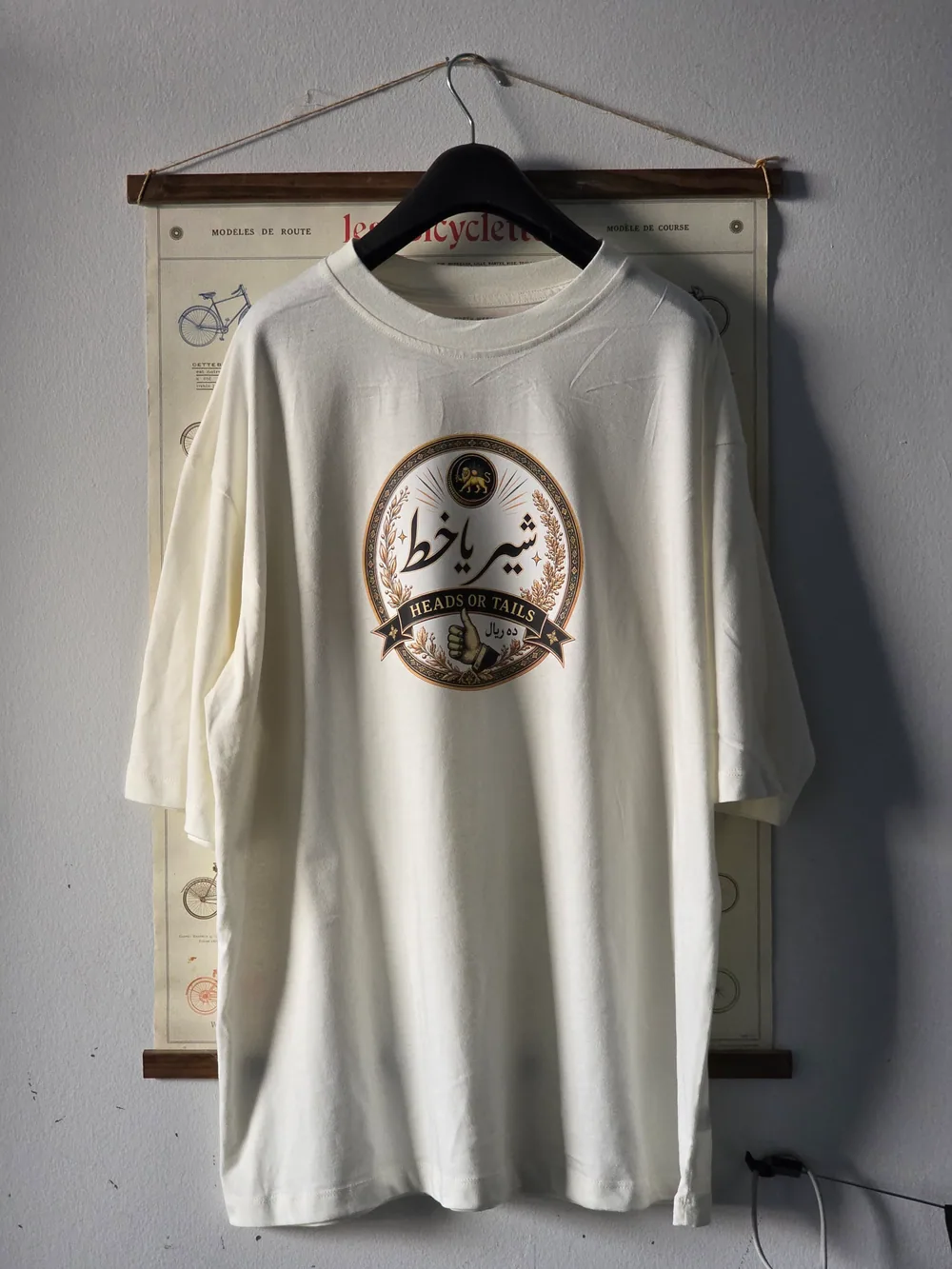 Finished white Shir ya Khat graphic T-shirt hanging against a vintage bicycle print